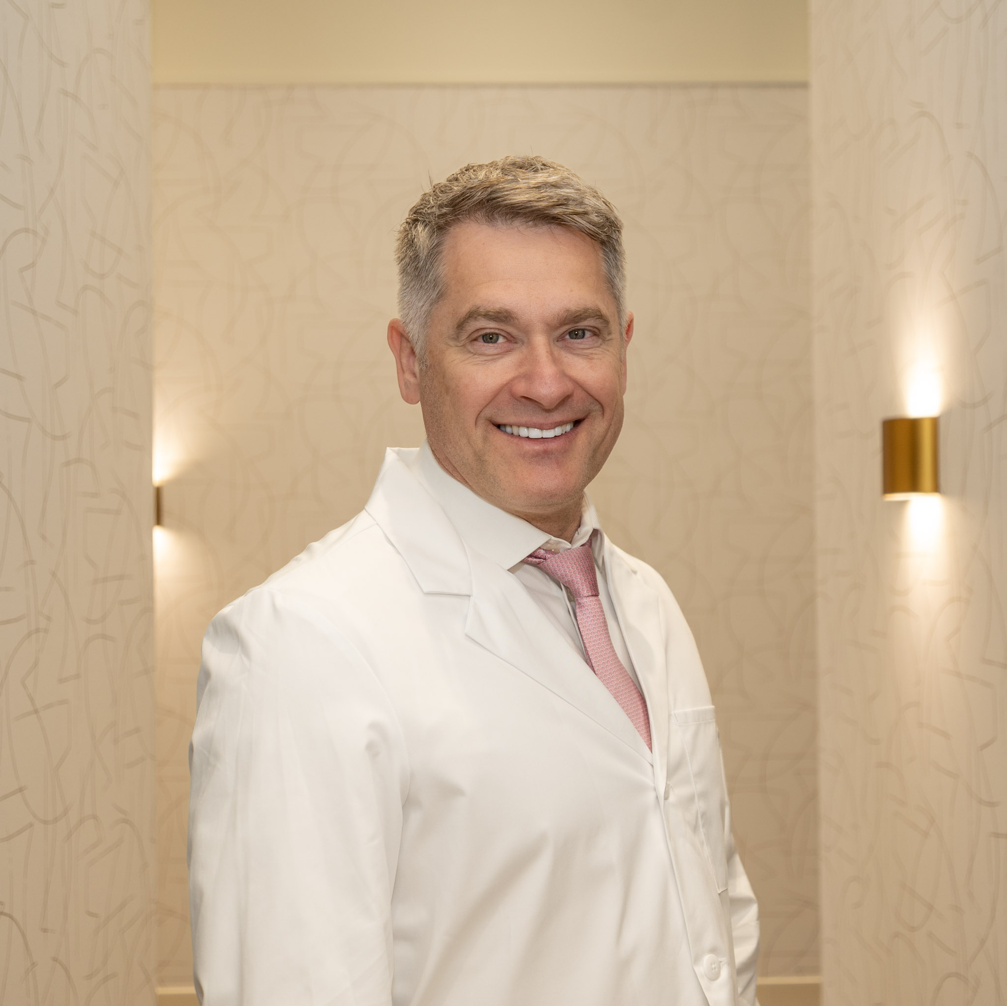 Dr. Perica Nonkovic, a family and sedation dentist at Spray Lake Dental in Cochrane, Alberta, smiling in a white dental coat.