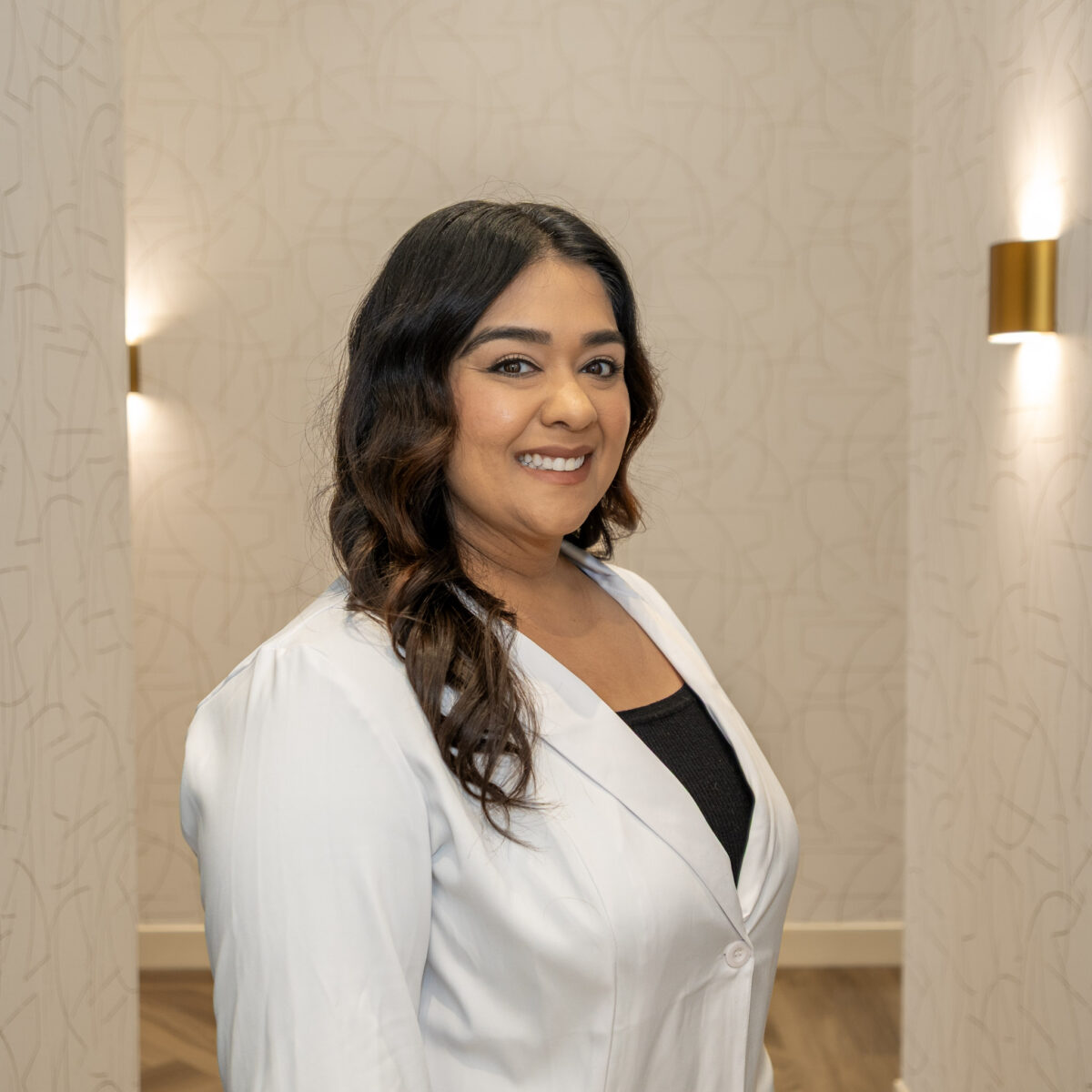 Dr. Ekta Cheba, a general and family dentist at Spray Lake Dental in Cochrane, Alberta, smiling in a white coat.