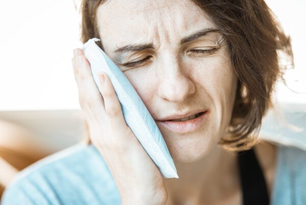 Person holding a blue ice pack to their cheek to reduce swelling after wisdom teeth removal in Cochrane.